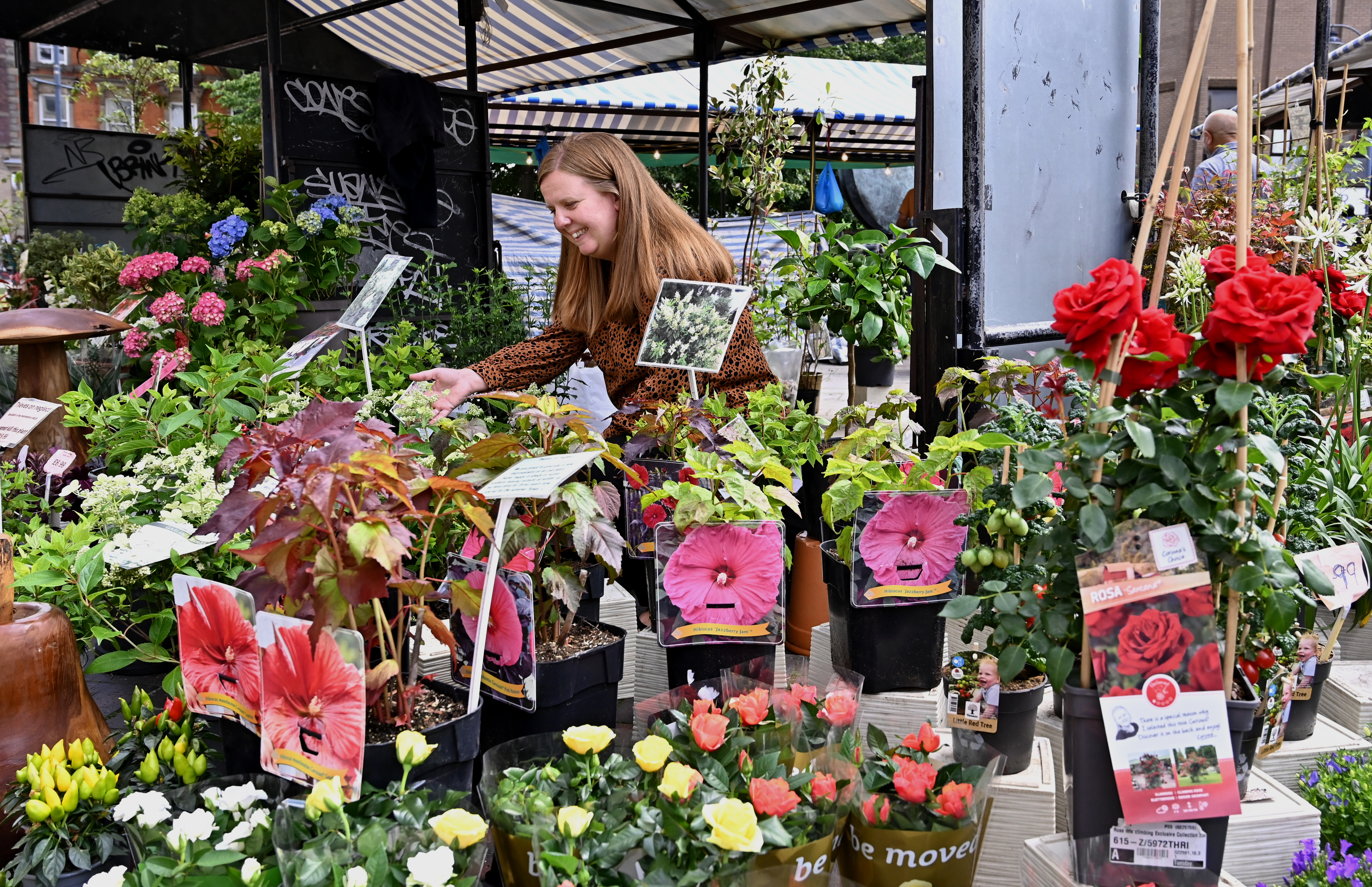 A smiling woman browsing plants and flowers at an outdoor market stall