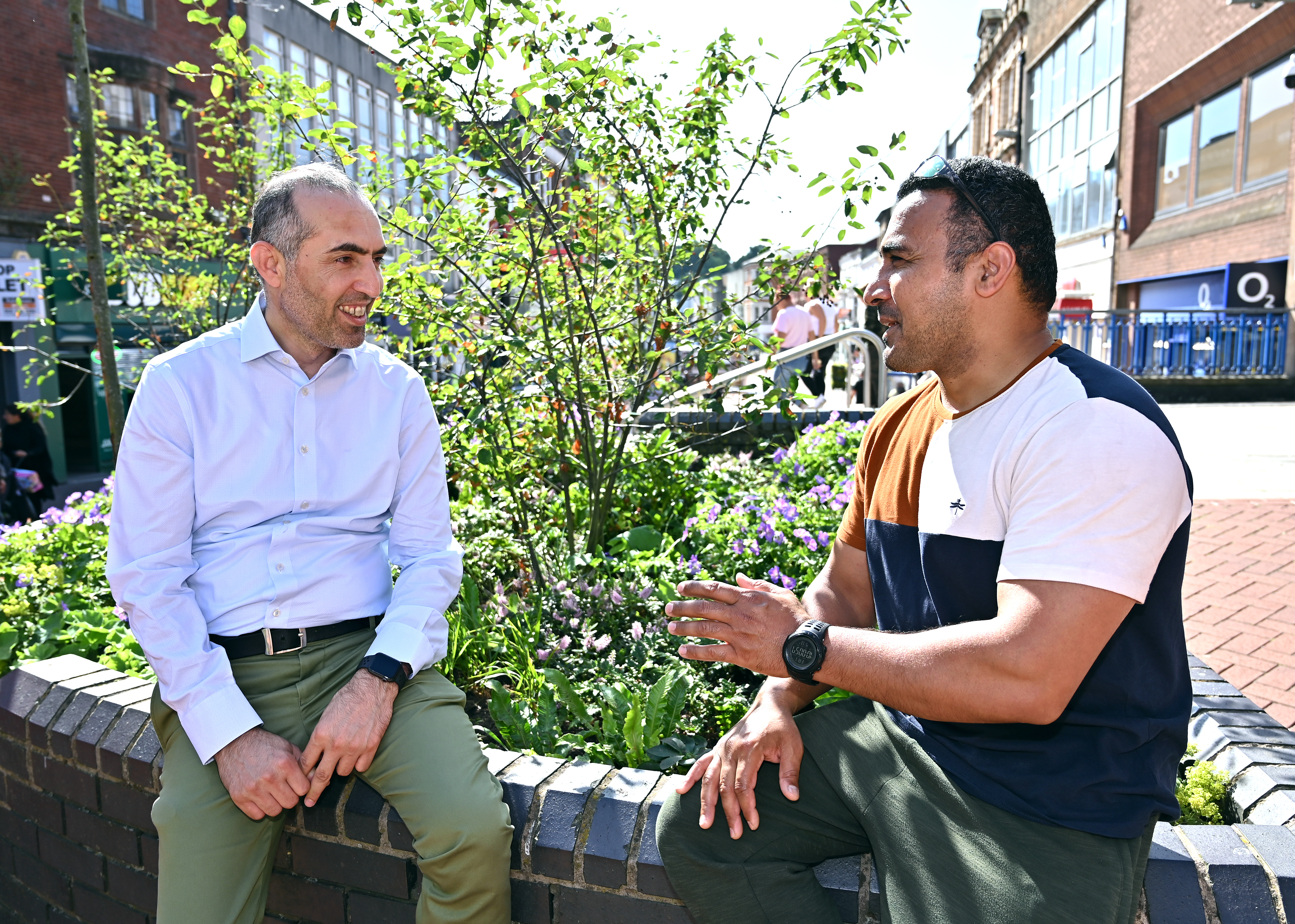 Two men sitting and talking near greenery and flowers in Walsall town centre