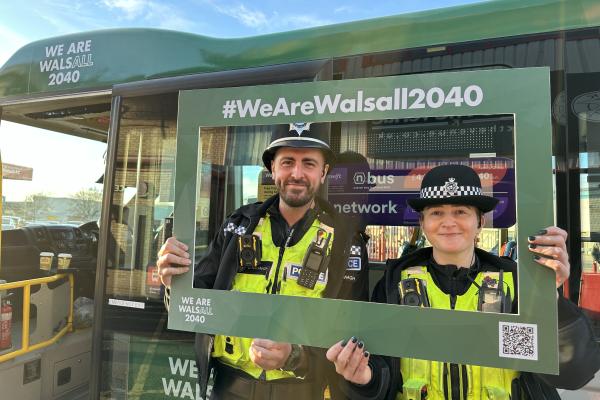 Two police officers smiling and holding a green frame with the hashtag #WeAreWalsall2040, standing in front of a green bus with 'We Are Walsall 2040' branding.